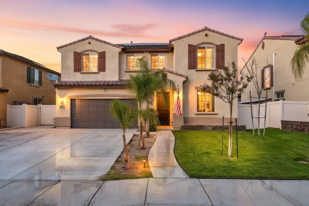Beautiful two-story house with well-lit windows, manicured lawn, and tropical landscaping, showcasing professional real estate photography to enhance property listings.
